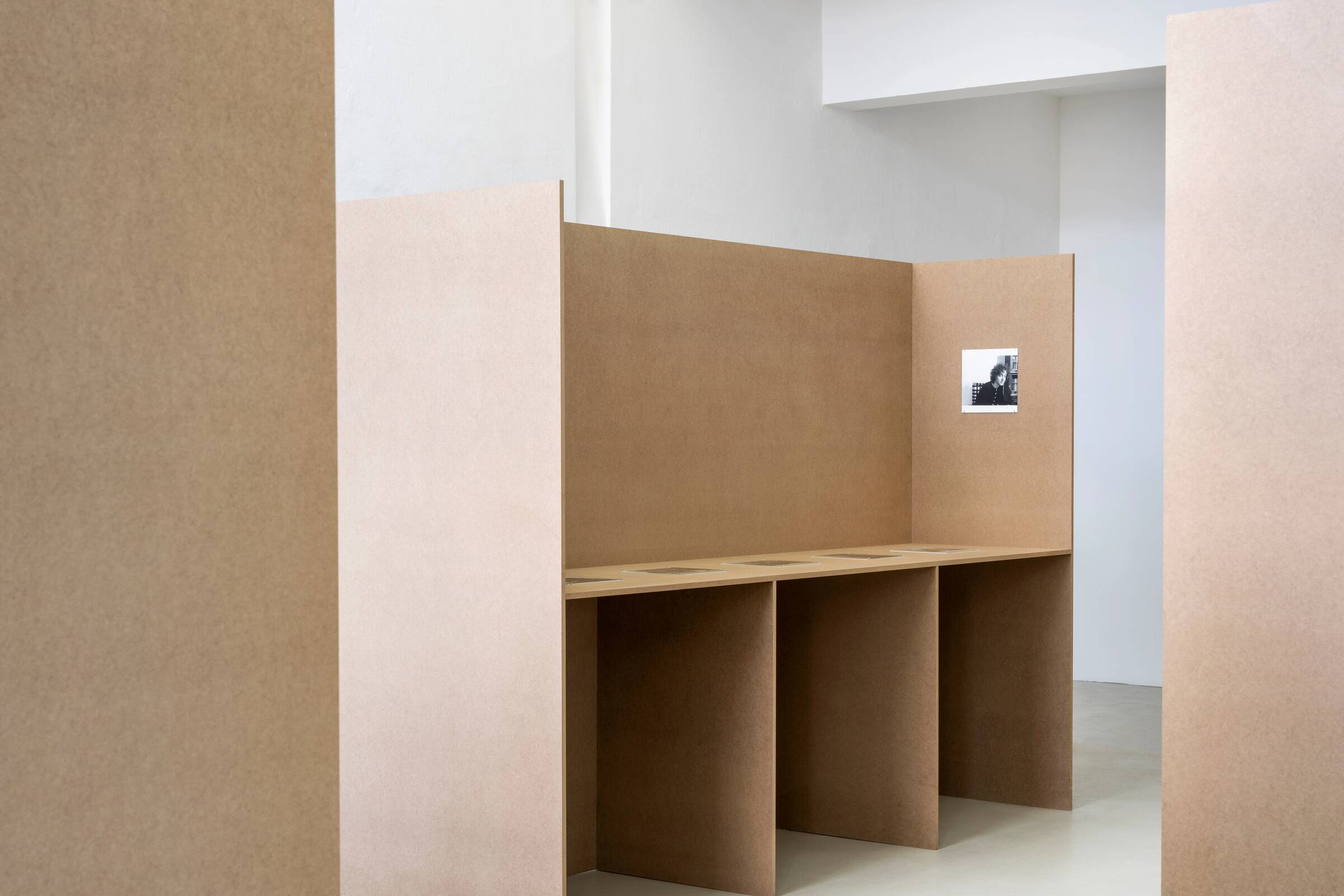 Drei braune, schlichte Trennwände, an einer Wand ein kleines schwarz-weißes Foto.