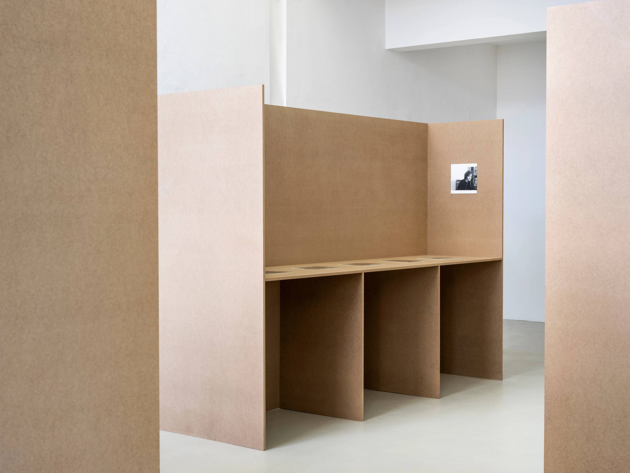 Drei braune, schlichte Trennwände, an einer Wand ein kleines schwarz-weißes Foto.