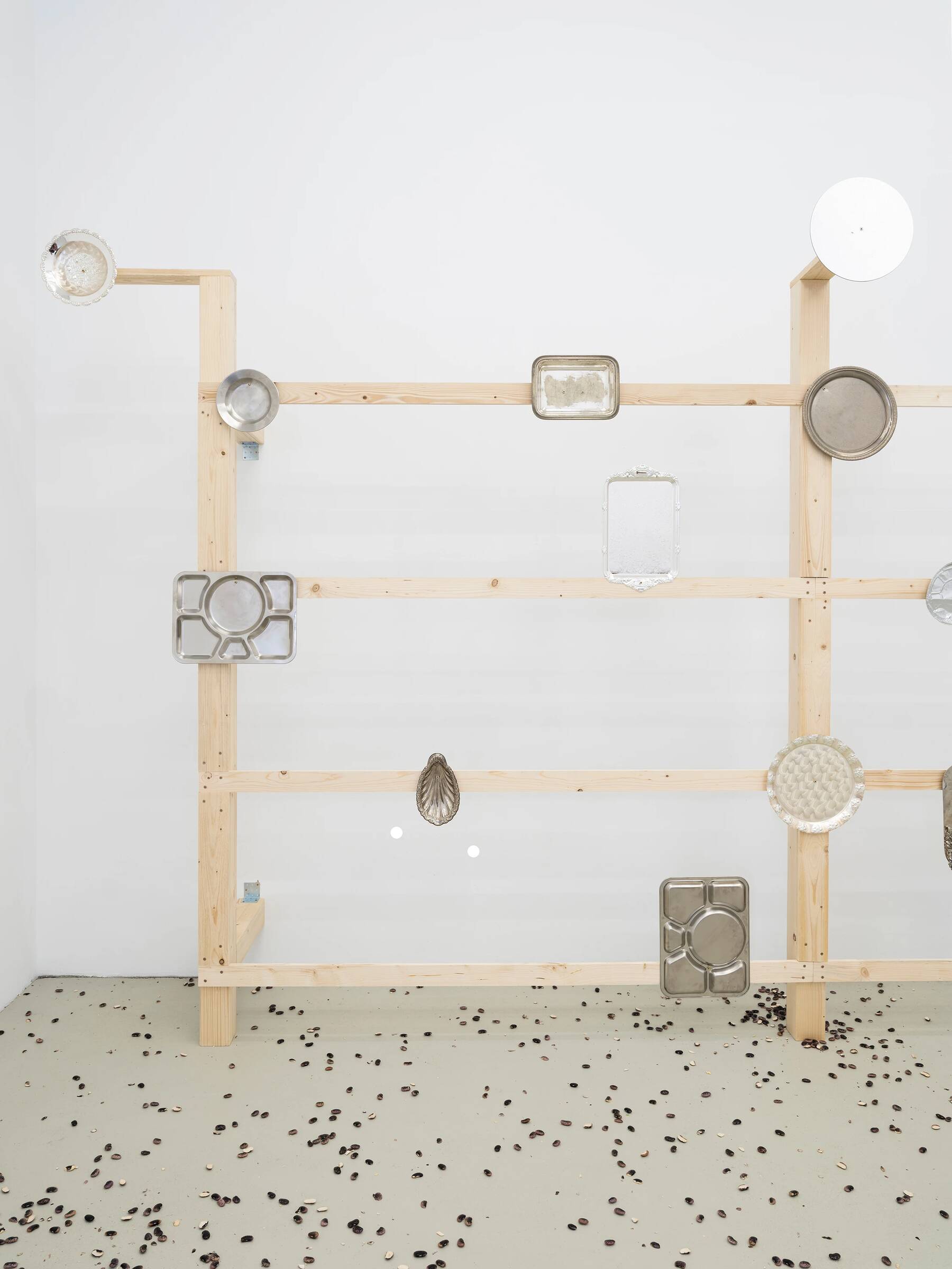 Holzregal mit mehreren angebrachten Metallbackformen in verschiedenen Formen und Größen, auf einem Boden mit verstreuten schwarzen Punkten.