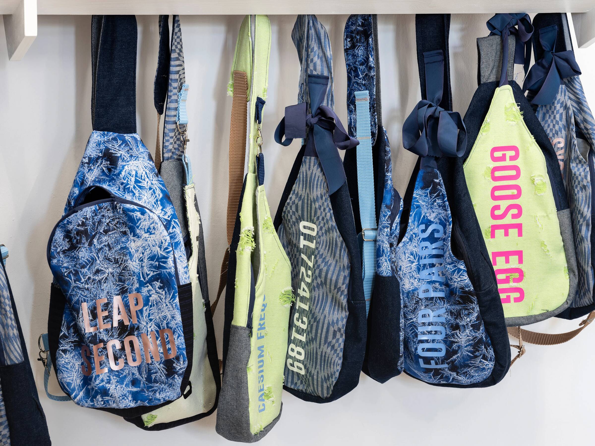 Mehrere bunte Rucksäcke mit unterschiedlichen Mustern und großen, farbigen Schriftzügen hängen nebeneinander an Haken.